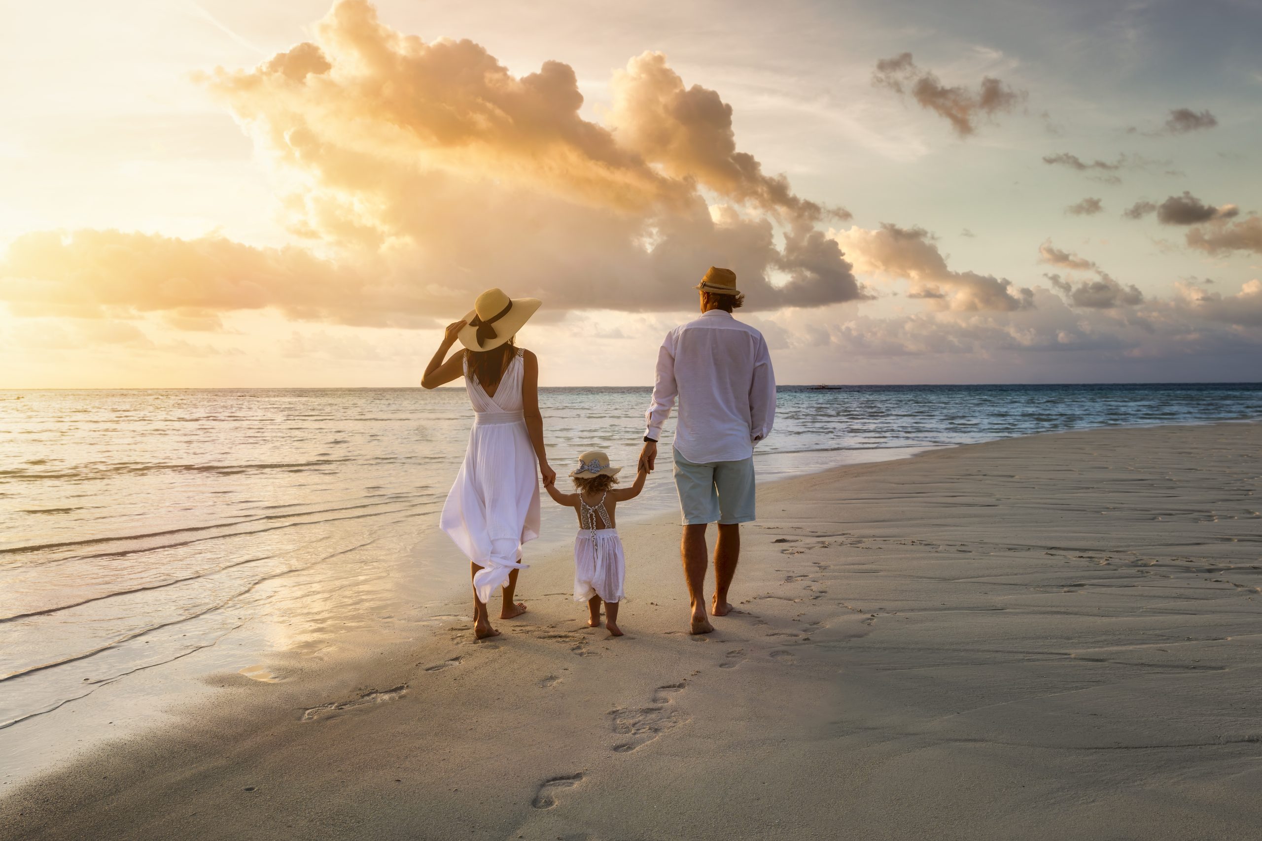 A family walks hand in hand down a tropical paradise beach during sunset